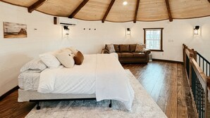 Un dormitorio con techo inclinado, vigas de madera, una cama, un sofá y una ventana.