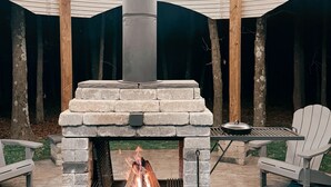 Un patio al aire libre con una chimenea de piedra, dos sillas Adirondack y una mesa.