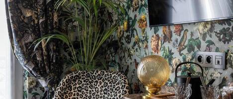 Een hoekappartement met een fauteuil met luipaardprint, een flatscreen-tv aan de muur, een klein tafeltje met een decoratieve schaal, en een groene poef.