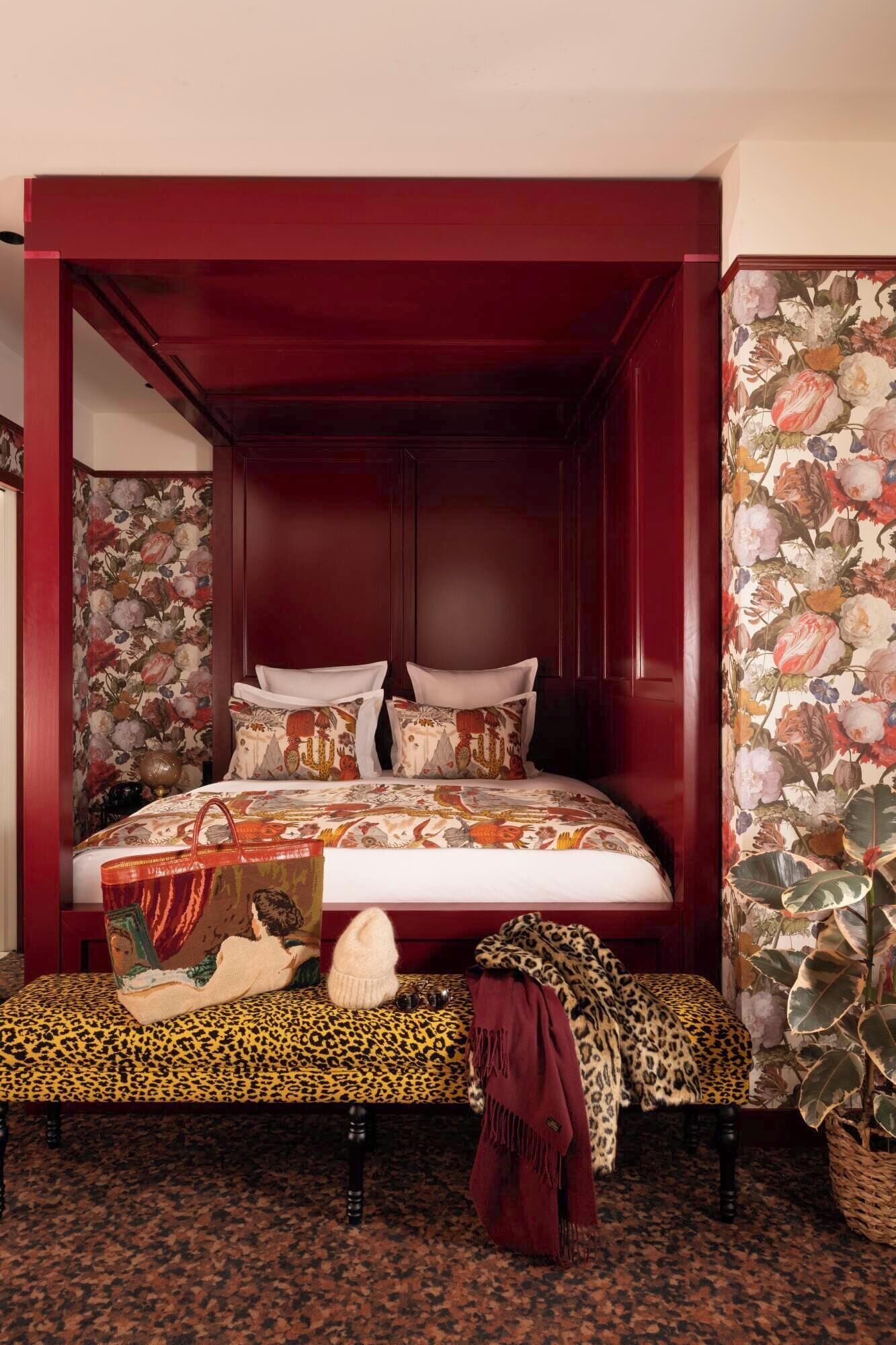 Un lit avec une tête de lit et un pied de lit ornés d’un motif floral, un banc à imprimé léopard et un plaid rouge.