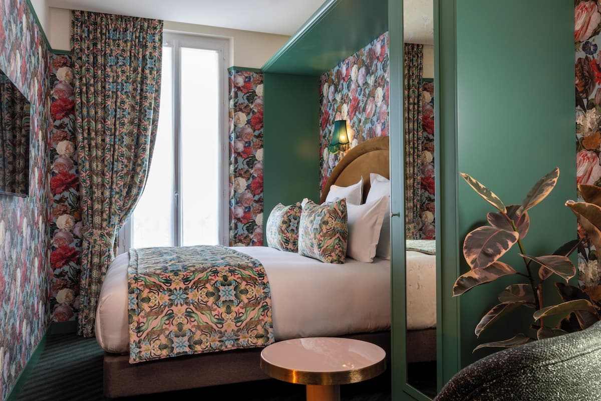A hotel room with a bed, a round table, and floral wallpaper.