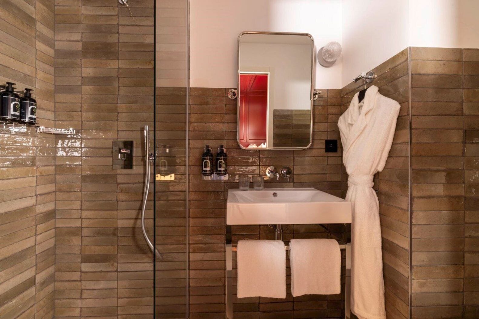 Een moderne badkamer met een douche met glazen wand, een witte wastafel met twee handdoeken en een badjas aan een rek.