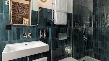 A modern bathroom with a white sink, a glass shower enclosure, and a mirror with a floral backsplash.