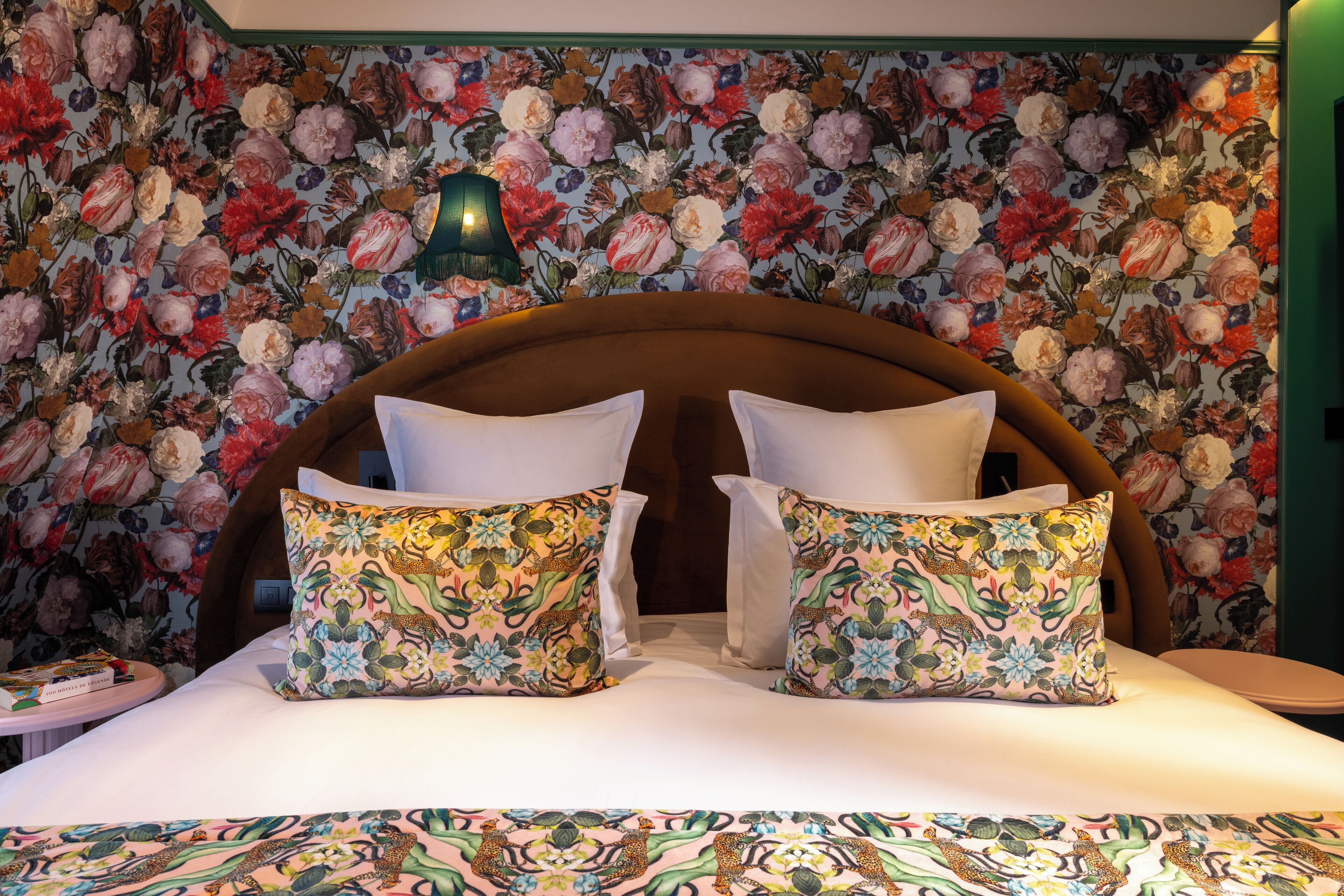 A bed with floral-patterned pillows and a headboard, set against a floral wallpaper backdrop.