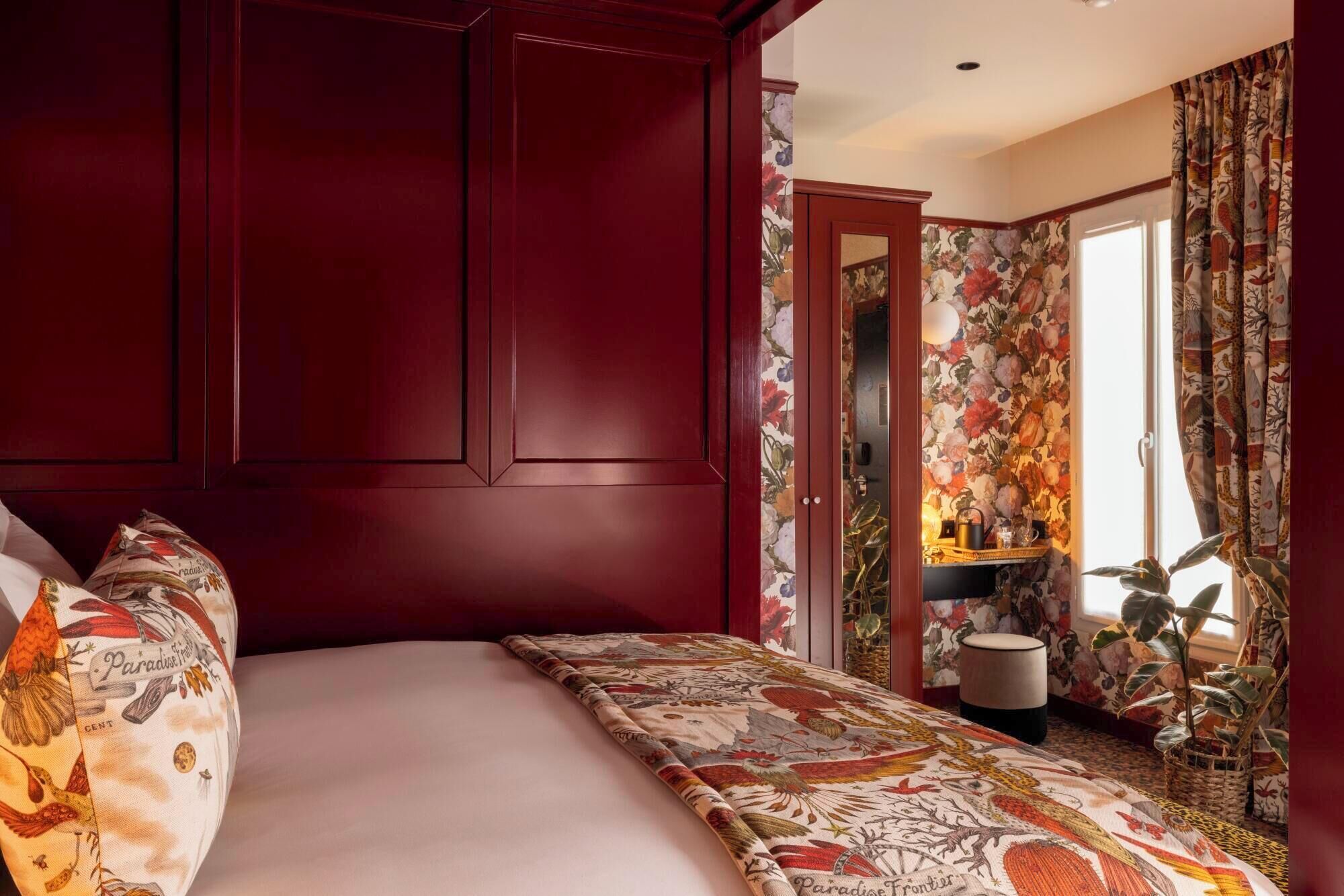 A bedroom with a large bed, floral wallpaper, and a red wardrobe.