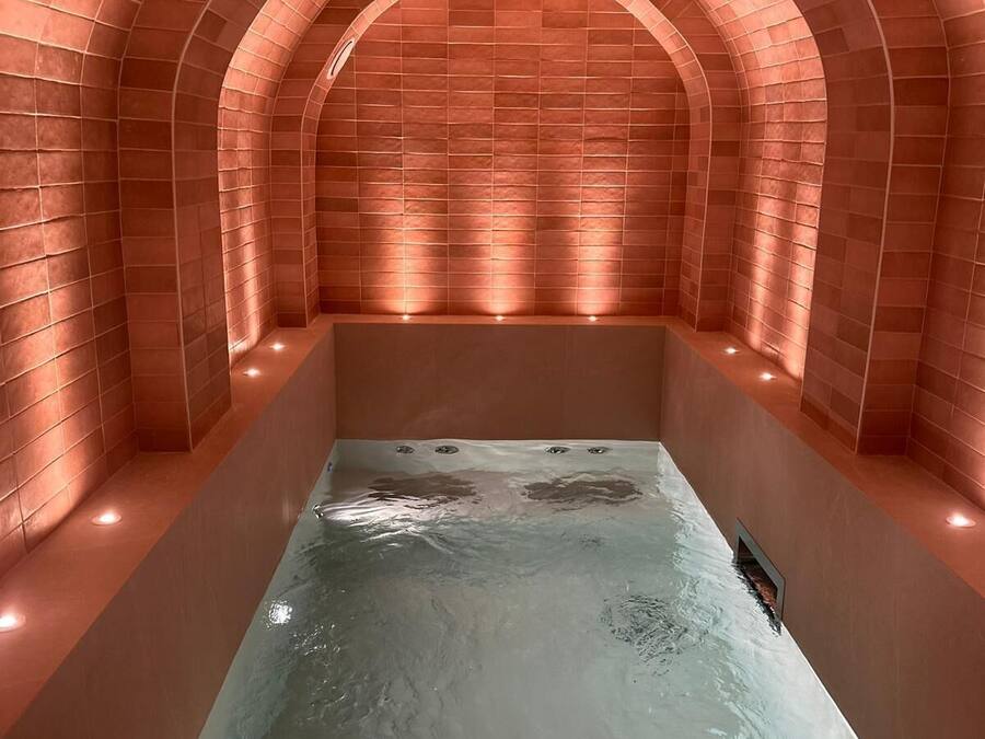 Une salle de spa dotée d’un jacuzzi rectangulaire, de murs en briques en arc de cercle et d’un éclairage encastré.