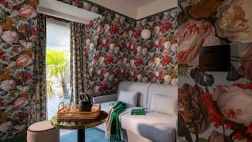 Una habitación con papel tapiz floral, un sofá, una mesita con una cesta y una planta en maceta.
