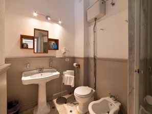 A bathroom with a pedestal sink, a toilet, a bidet, and a shower.