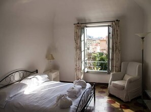 A bedroom with a bed, a chair, a nightstand, a lamp, and a window with curtains.