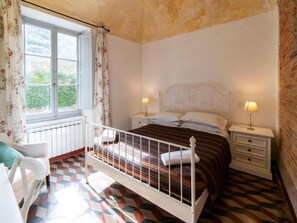 Un dormitorio con cama, dos mesitas de noche, una ventana con cortinas y un radiador.