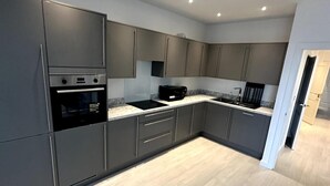 A modern kitchen with grey cabinets, a built-in oven, and a microwave. - Frogley Park Cozy Apartment (Barking)