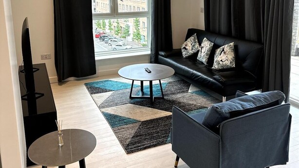 A modern living room with a black sofa, a round coffee table, and a grey armchair. - Frogley Park Cozy Apartment (Barking)