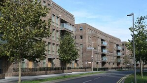 A multi-story residential building with a brick facade, balconies, and a clear road in front. - Frogley Park Cozy Apartment (Barking)