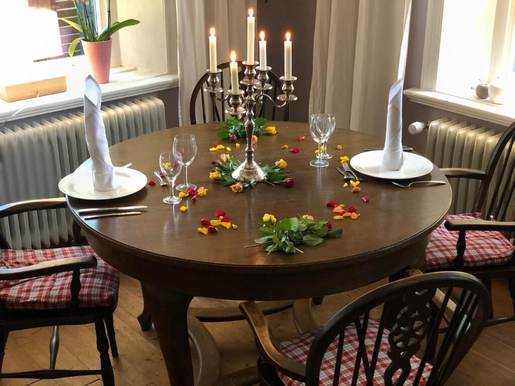 Una mesa redonda de comedor con velas, copas y pétalos de flores.