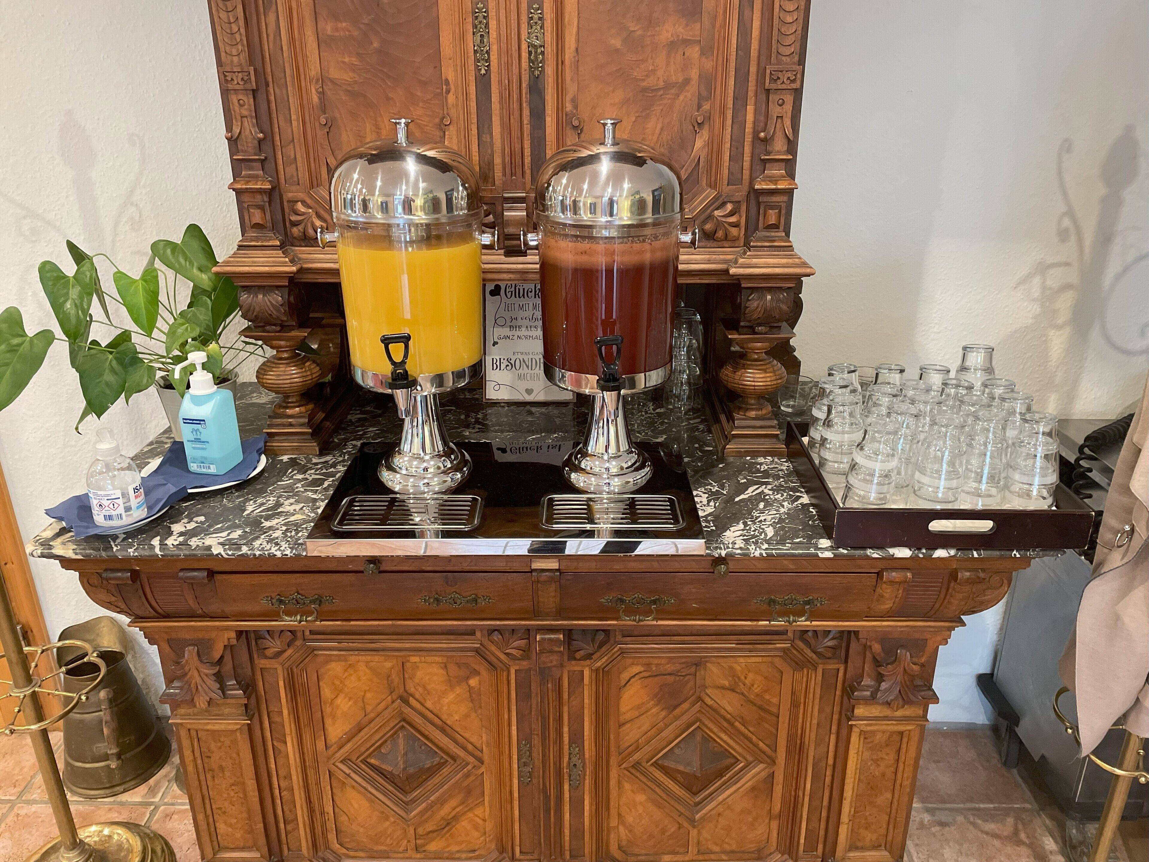 Un espace bar équipé de deux distributeurs de boissons, d’une plante en pot et d’un plateau de verres.