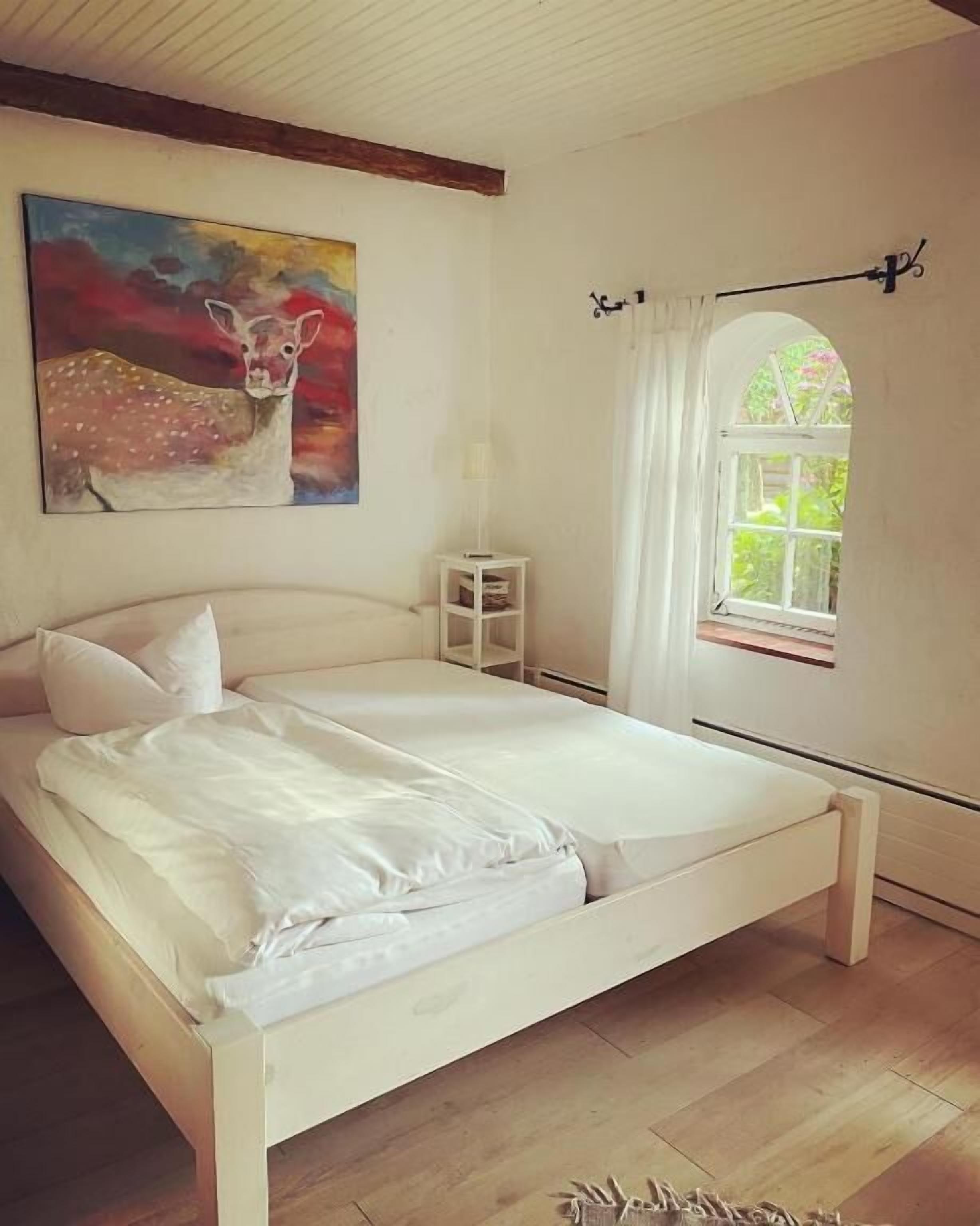 Een slaapkamer met een bed, een schilderij, een raam en een klein nachtkastje.