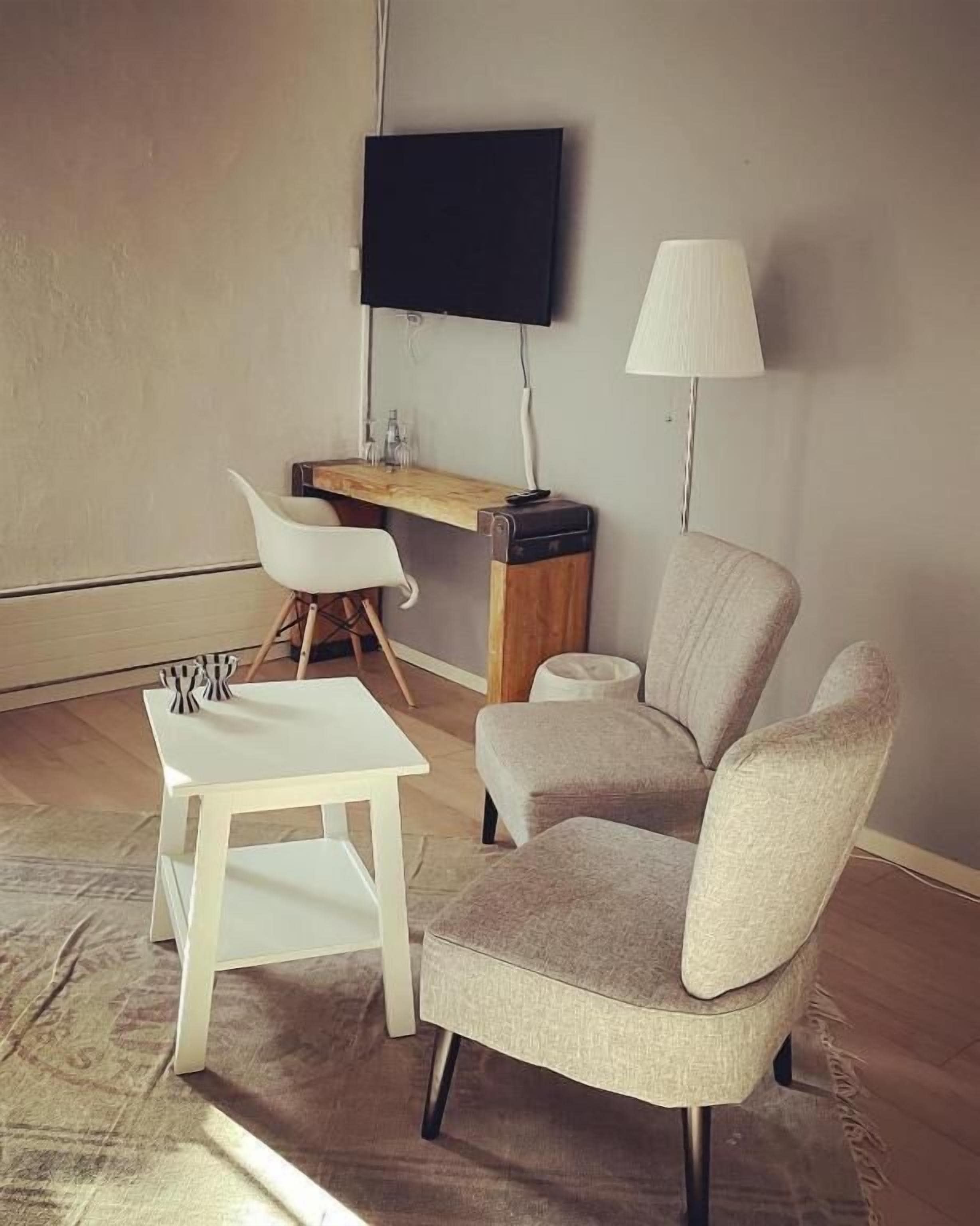 Una sala de estar moderna con una mesa blanca, un sillón color beige, un escritorio de madera y un televisor montado en la pared.