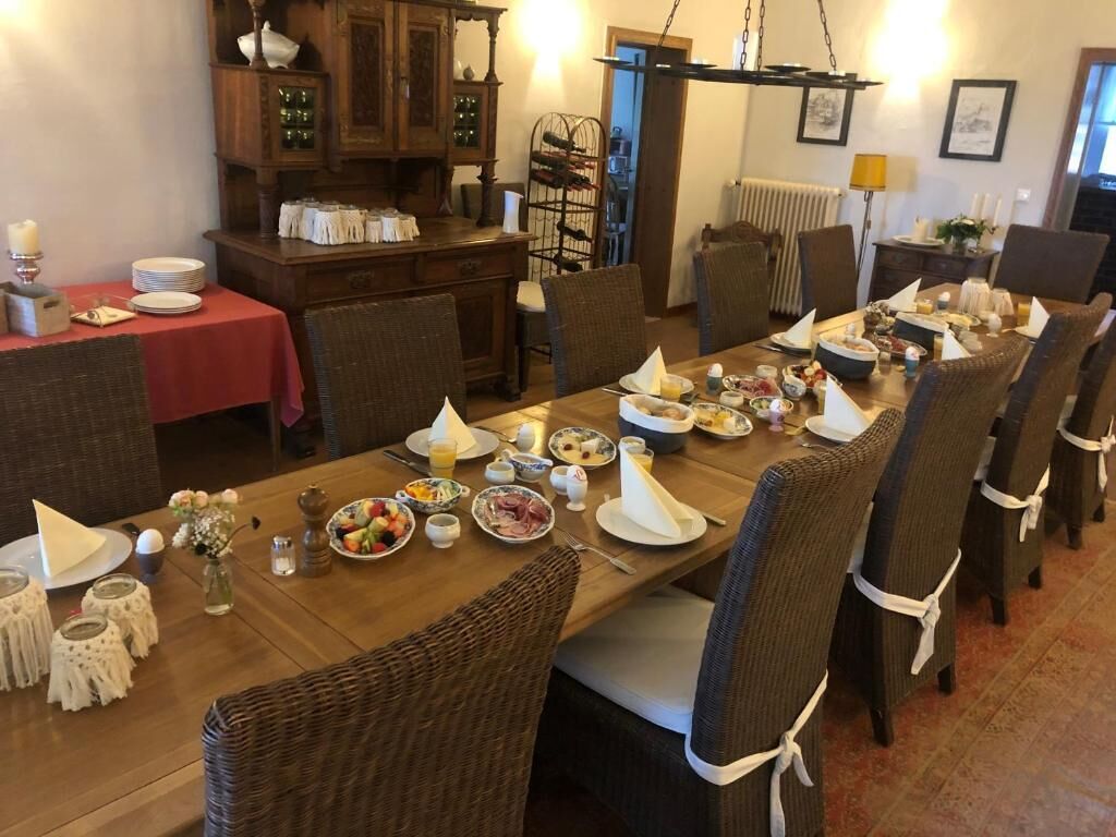 A dining area with a long wooden table set for a meal, surrounded by wicker chairs.