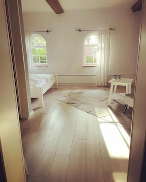 Une pièce comprenant un lit, une petite table, deux fenêtres avec des rideaux et un radiateur.