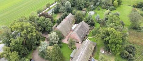 An aerial view of a property with a central building surrounded by trees, a parking area with cars, and a field in the background.