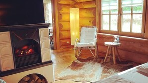 Ein gemütliches Blockhaus-Interieur mit Kamin, Schaukelstuhl und kleinem Tisch am Fenster.