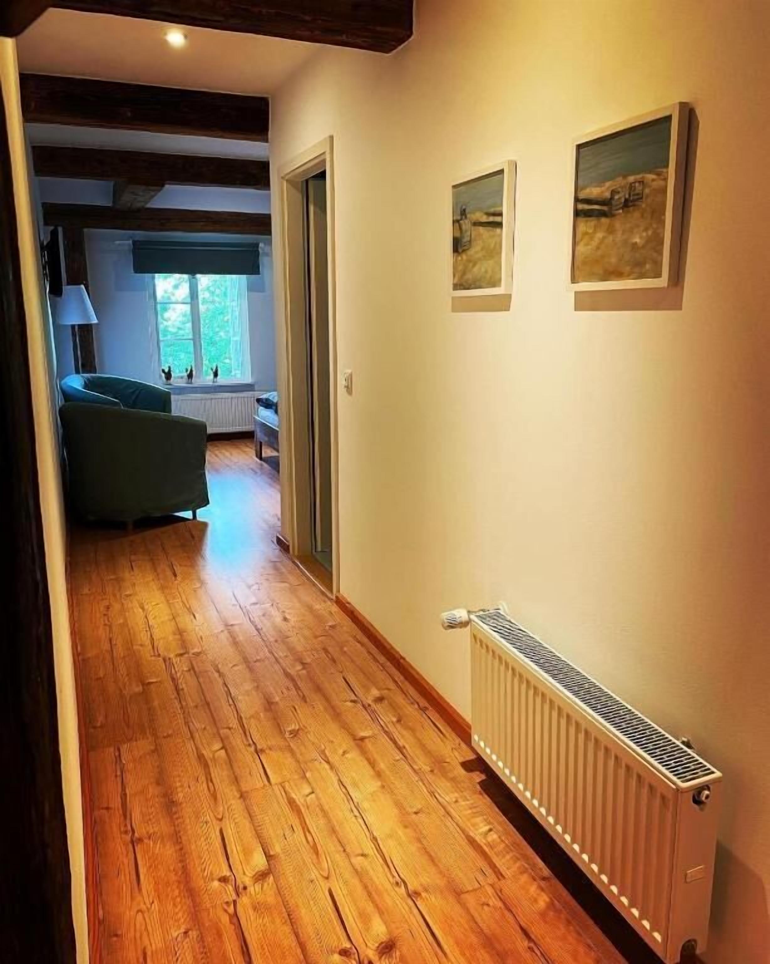 A hallway with wooden flooring, a radiator, and two framed pictures on the wall.