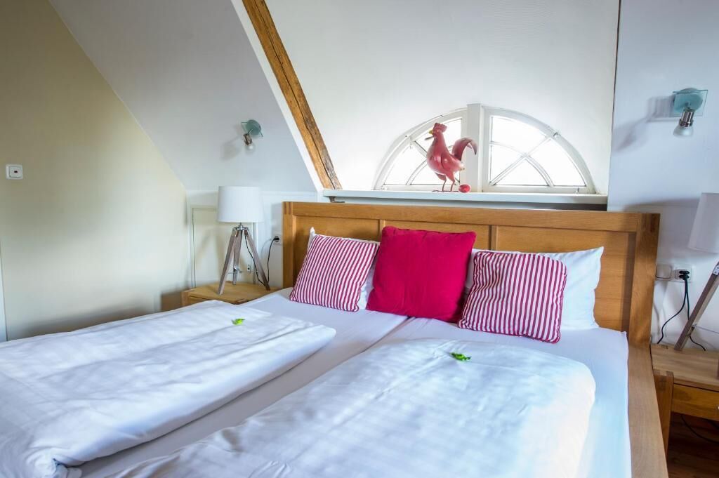 Un dormitorio con dos camas, cabecero de madera, tragaluz con adorno de gallo y una ventana.