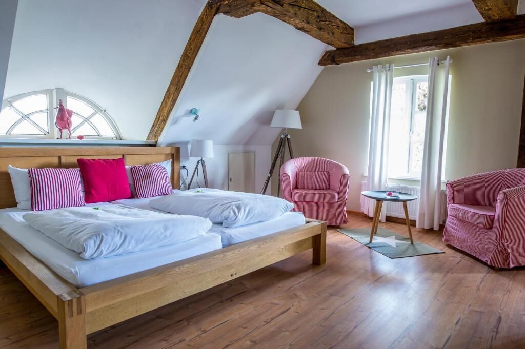 Ein Schlafzimmer mit einem hölzernen Bett, einem Fenster mit Vorhängen, einer Lampe und einem Sessel.