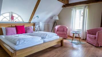Ein Schlafzimmer mit einem hölzernen Bett, einem Fenster mit Vorhängen, einer Lampe und einem Sessel.