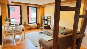A cozy living room with wooden flooring, a brown sofa, a white chair, and a dining table. - Großes Apartment an der Loreley (Sankt Goar)