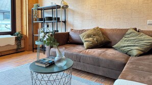 A cozy living room with a brown leather sofa, a small round coffee table, and a bookshelf against a textured wall. - Großes Apartment an der Loreley (Sankt Goar)