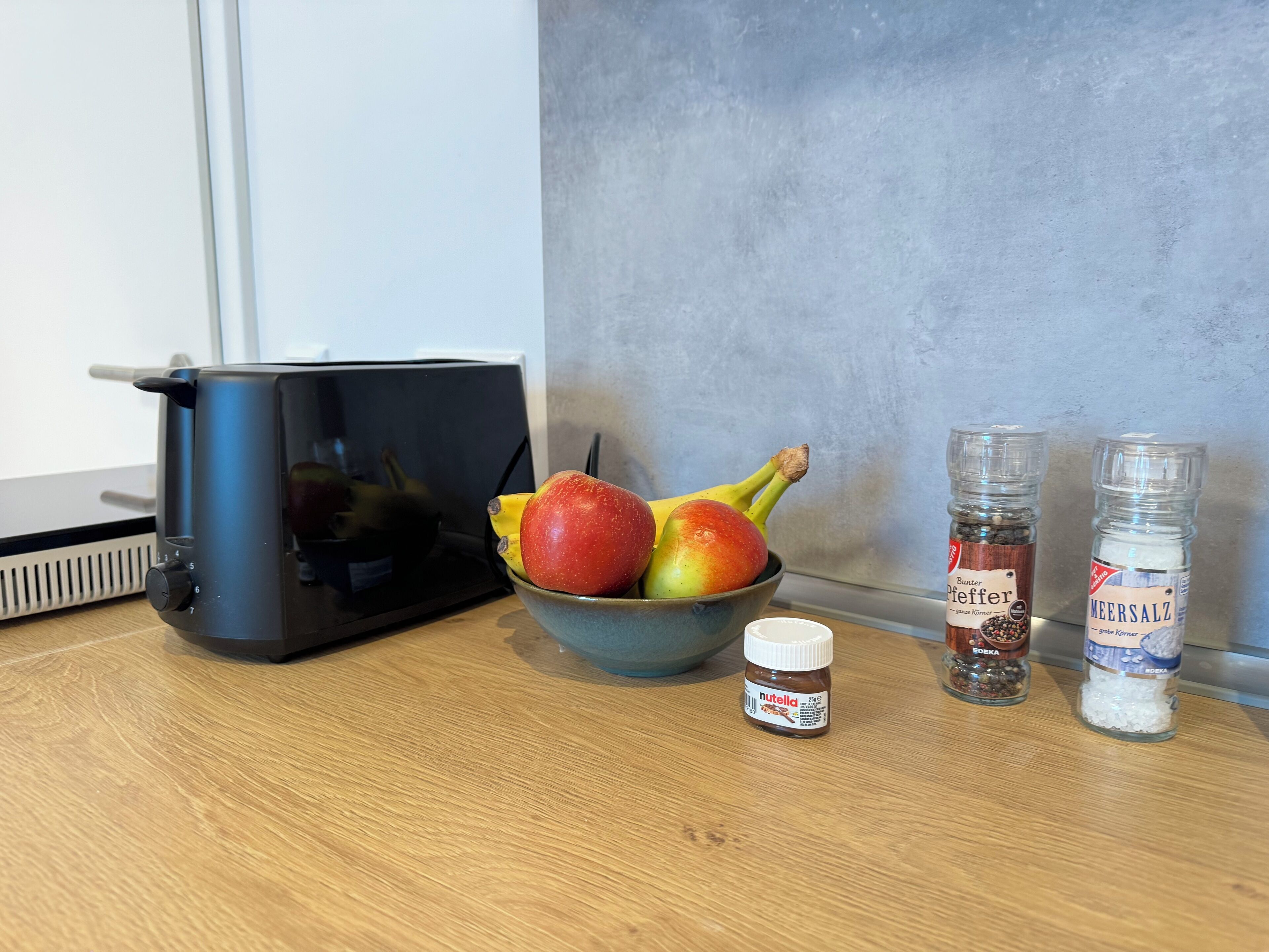 A kitchen counter with a bowl of fruit, a Nutella jar, and two spice jars.