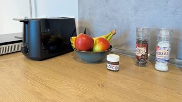 A kitchen counter with a bowl of fruit, a Nutella jar, and two spice jars.