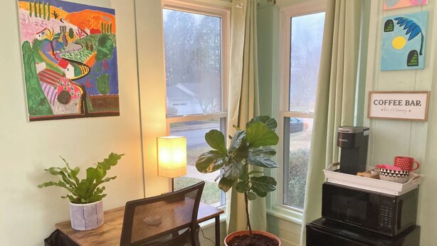 Une petite pièce agréable, dotée d’un bureau, d’une chaise, de plantes en pot, d’un coin café et d’un four à micro-ondes.
