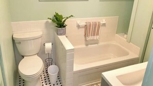 Une salle de bain comprenant des toilettes, un lavabo, une baignoire et une fenêtre ornée d’un motif géométrique.