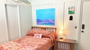 Une chambre à coucher avec un lit, une table de chevet, une commode, un tableau et une porte.