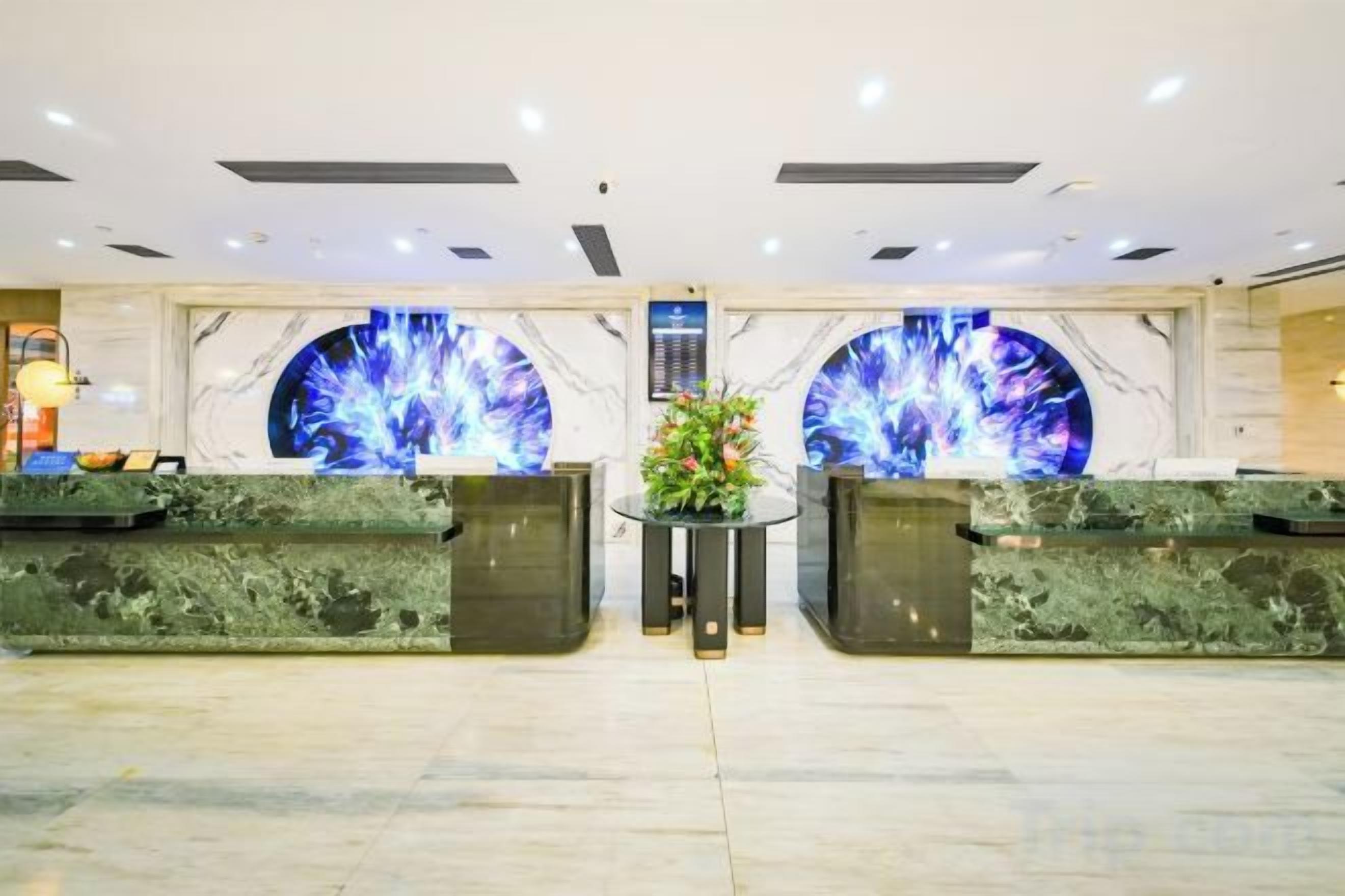 Een hotel receptie met marmeren balies en twee grote ronde schermen waarop een abstract blauw ontwerp wordt getoond.
