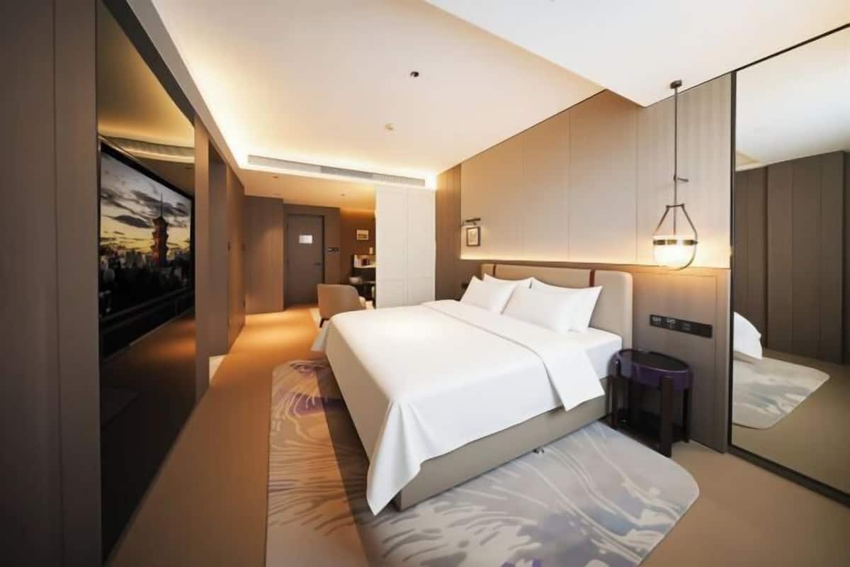 Ein modernes Hotelzimmer mit einem großen Bett, einem Nachttisch, einem Spiegel und einem am Wand montierten Fernseher.