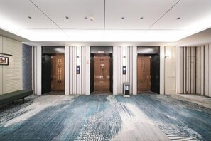 Un hall d’hôtel avec trois ascenseurs, une moquette à motifs et un banc.
