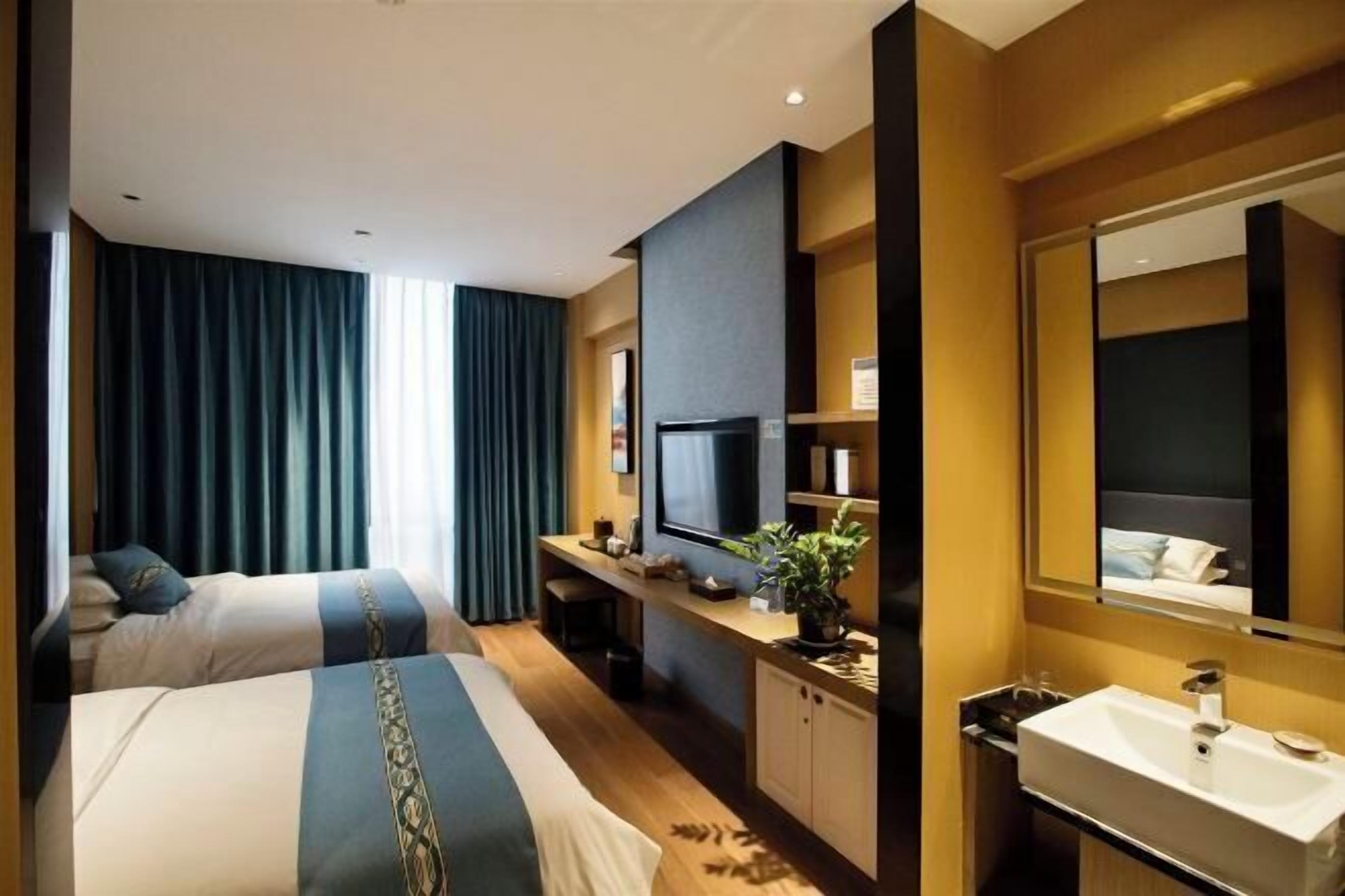 Habitación de hotel con dos camas, un escritorio con televisor, un espejo grande y un baño con lavamanos y espejo.