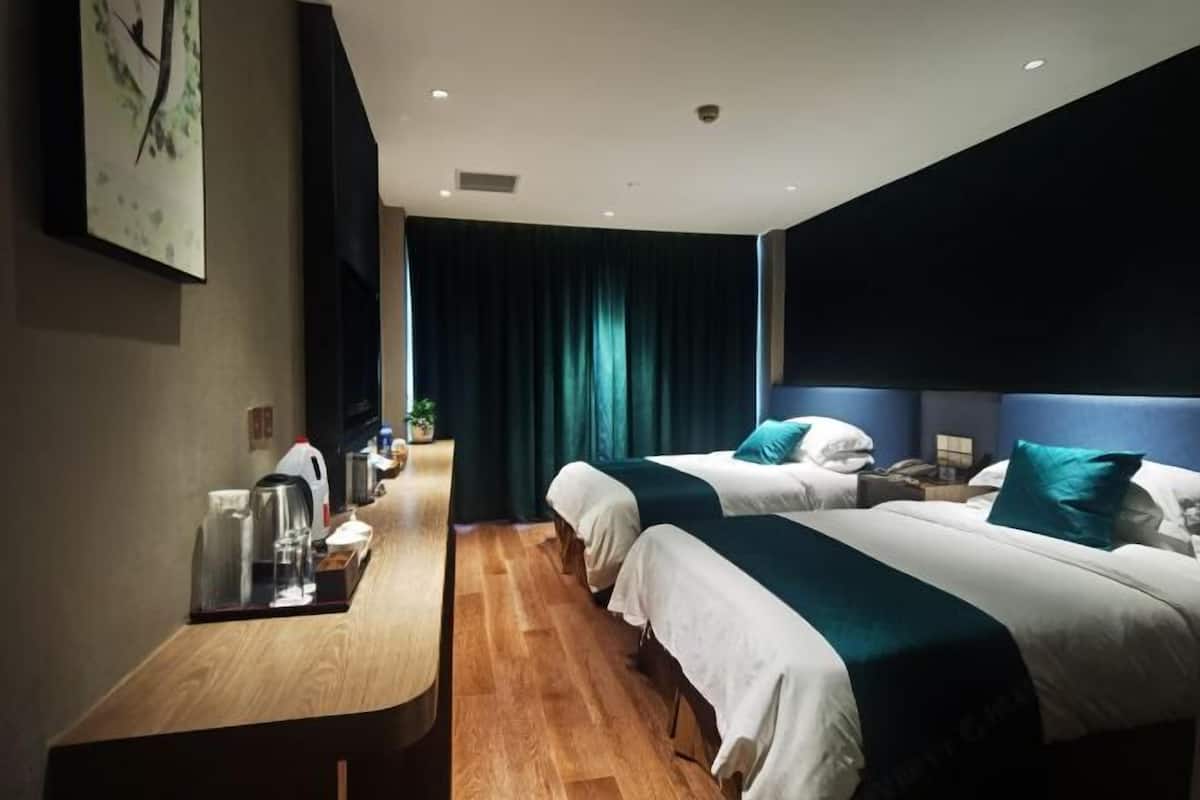 Ein Hotelzimmer mit zwei Betten, einem Holztisch, einem Nachttisch und einem großen Fenster mit Vorhängen.