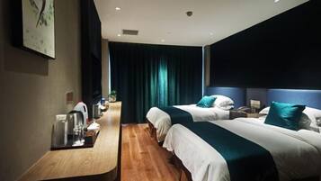 A hotel room with two beds, a wooden desk, a nightstand, and a large window with curtains.