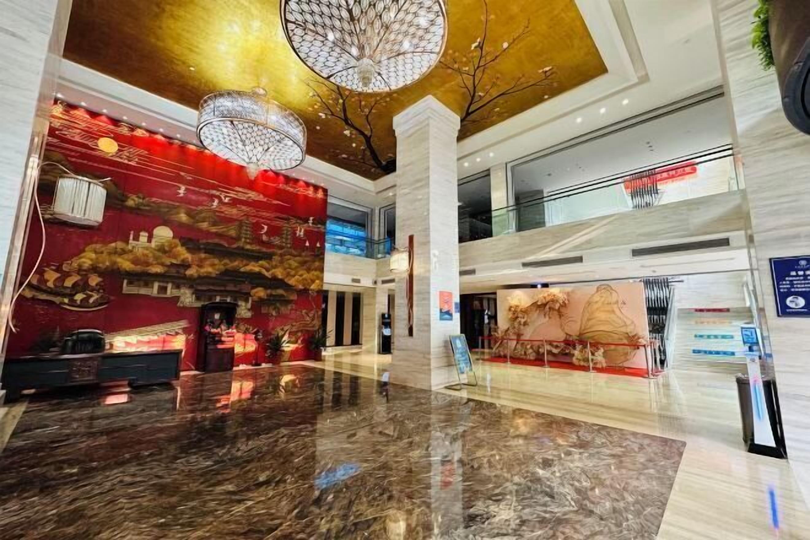 A spacious lobby with a marble floor, a red wall with cultural artwork, and a gold ceiling.