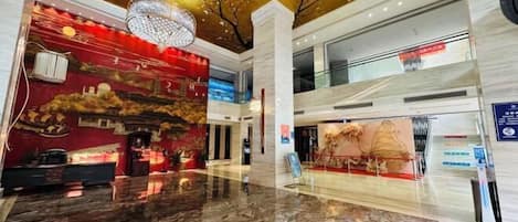 A spacious lobby with a marble floor, a red wall with cultural artwork, and a gold ceiling.