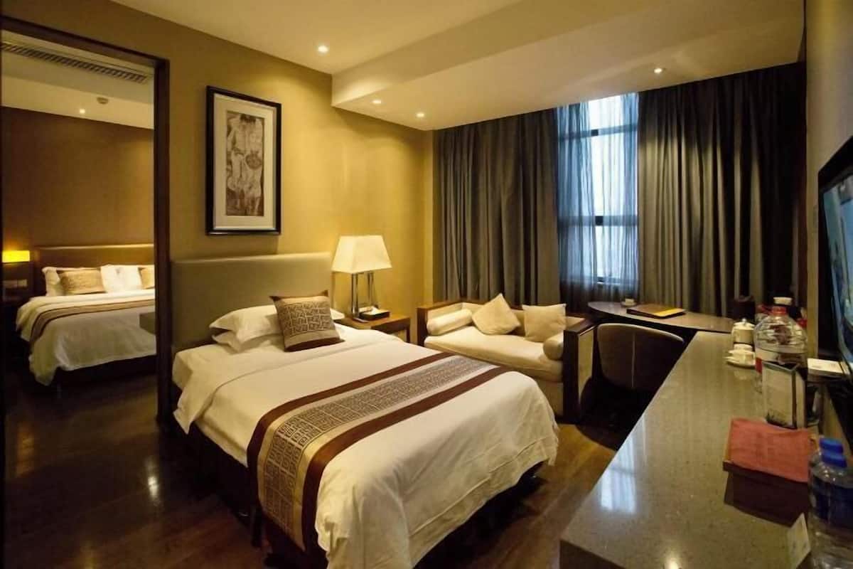Ein Hotelzimmer mit zwei Betten, einem Schreibtisch, einem Sessel, einem Fernseher und einem großen Fenster mit Vorhängen.