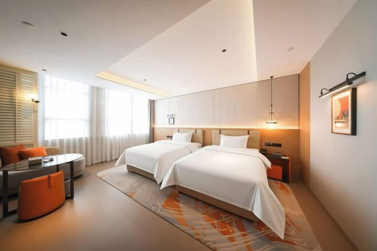 Ein modernes Hotelzimmer mit zwei Betten, einem Schreibtisch und einem Sofa.
