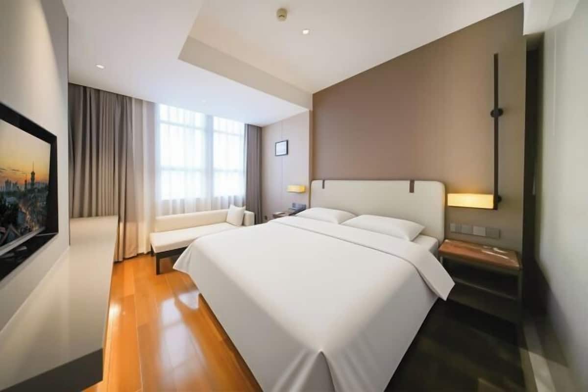 Ein modernes Hotelzimmer mit einem großen Bett, einer Couch, einem Fernseher und einem fenster mit Vorhängen.