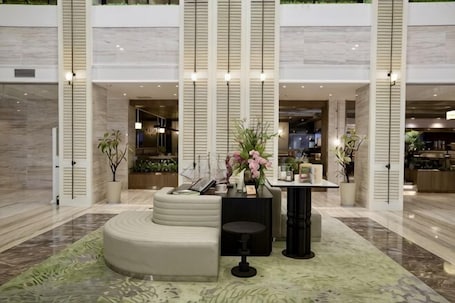 A lobby with a curved seating area, a small table with a vase, and a large mirror.. Peninsula International Hotel