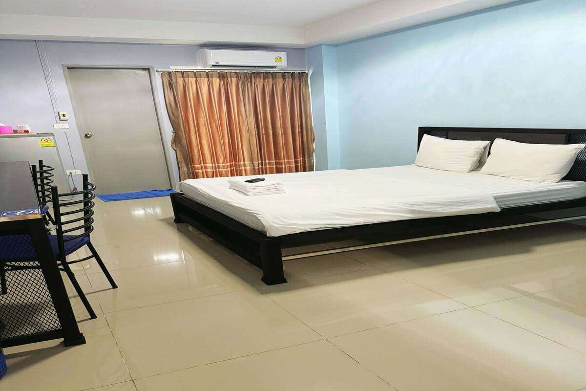 A hotel room with a bed, a desk, and an air conditioning unit.