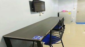 A long table with blue chairs, a television mounted on the wall, and a refrigerator in the background. - OYO 75506 Ratchapruek Apartment Suphanburi  (Suphan Buri)